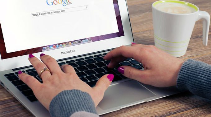 Osoba píše na notebooku s otevřeným vyhledávačem Google, vedle stojí hrnek s kávou.