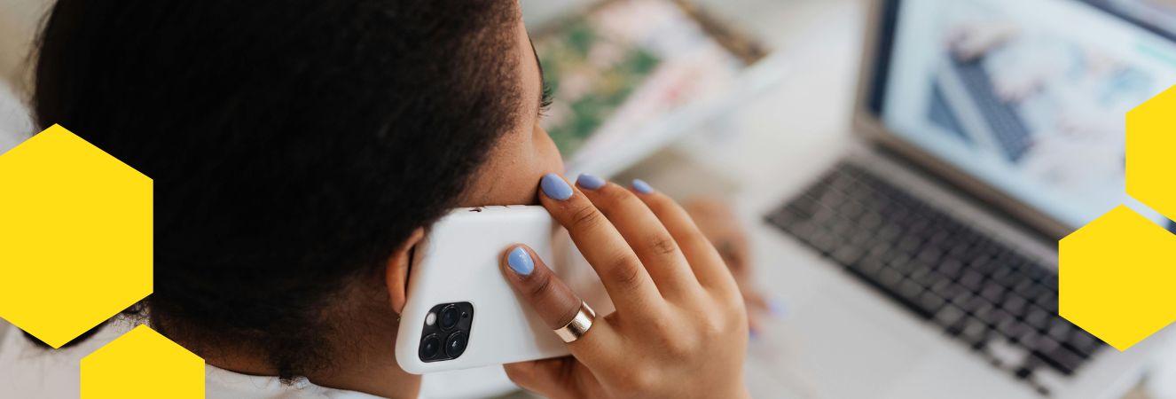 Žena s telefonem u ucha sedí u notebooku a pracuje. Na okrajích obrázku jsou žluté hexagony inspirované včelím motivem.