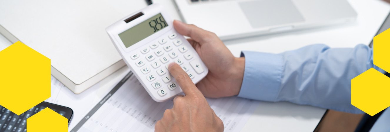 Osoba počítající PNO na kalkulačce, pracovní stůl s počítačem a dokumenty.