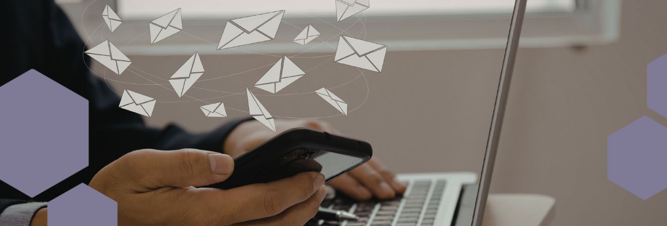 Muž drž&iacute; v ruce mobiln&iacute; telefon a druhou rukou p&iacute;&scaron;e na notebooku.